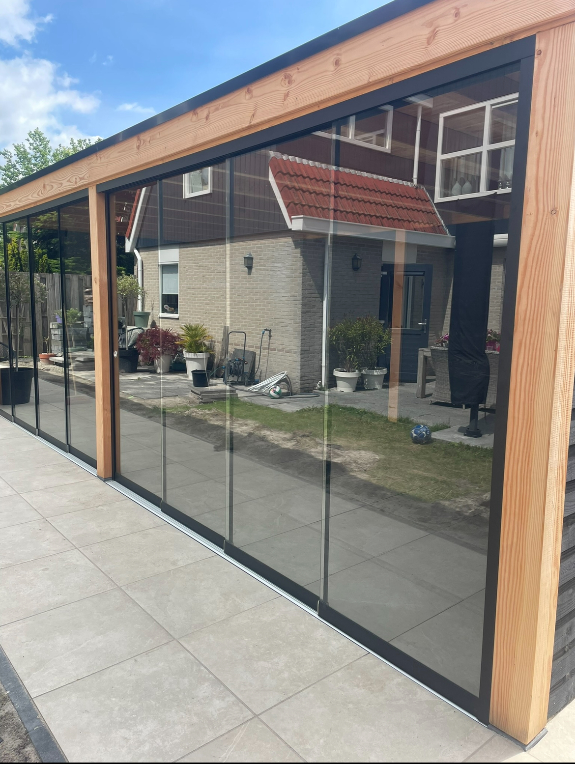 Glazen schuifwanden met antraciet profielen onder een houten overkapping